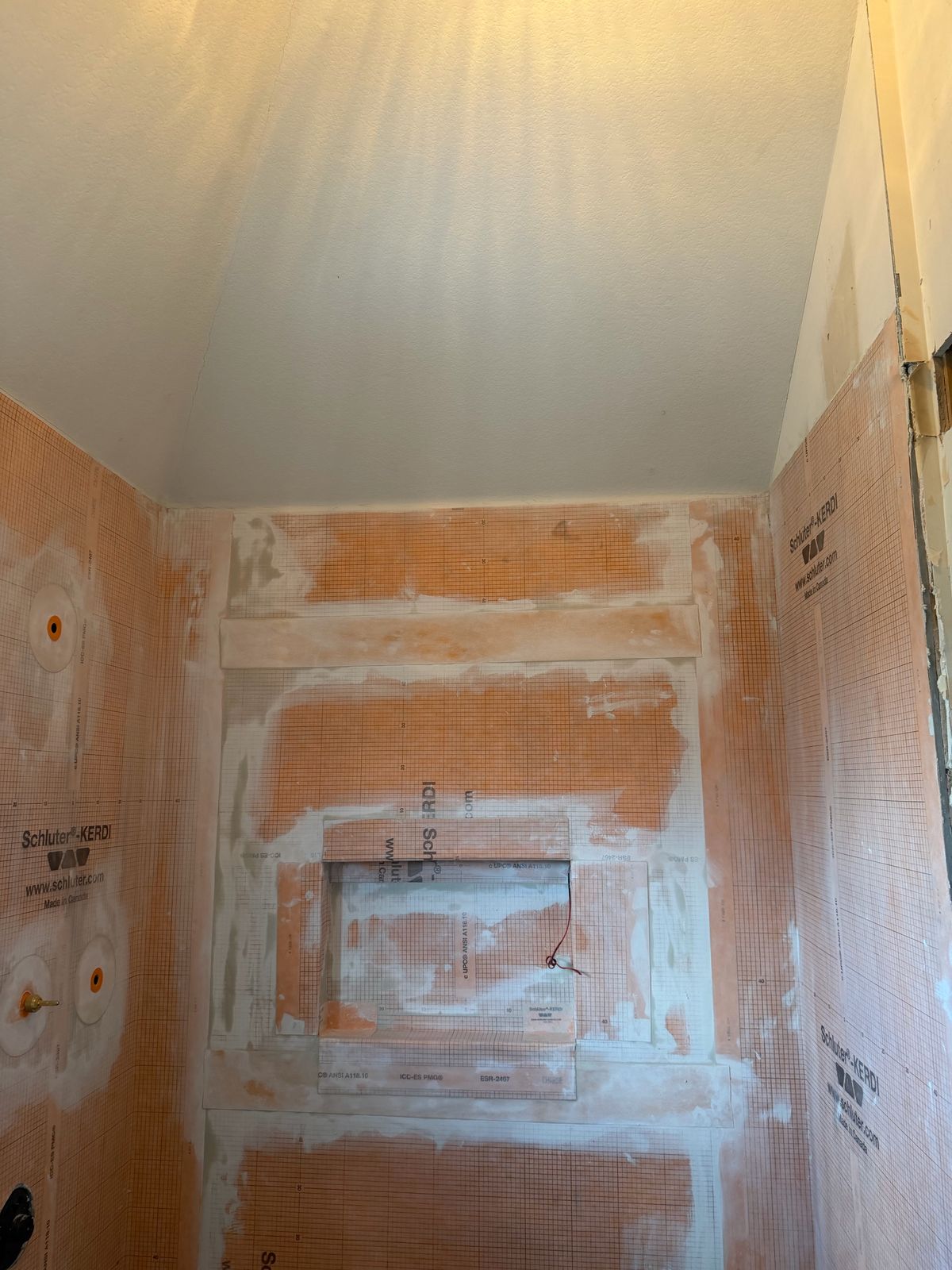 A Rexuvo shower waterproofed with orange Schluter KERDI, including the built-in niche, before any tile goes on